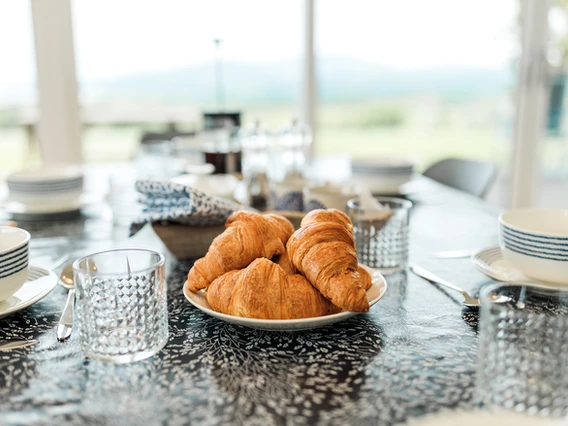 An elegant wooden table adorned with exquisite tableware, set within the opulent interior of our luxury lodge, inviting guests to indulge in a memorable dining experience surrounded by sophistication and comfort